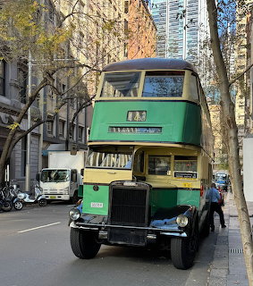 Green vintage double-decker bus on city street with buildings and trees