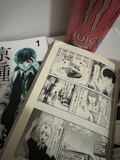 Open manga book with black and white panels next to a dark covered manga volume and a juice box