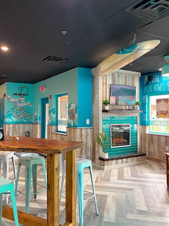 Turquoise cafe interior with wooden table, stools, surfboard, and fireplace wall