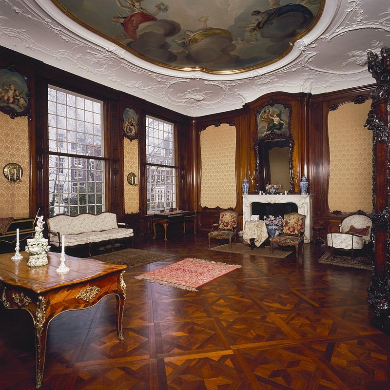 Historic interior room with painted ceiling, tall windows, wood paneling, ornate furniture and herringbone floor