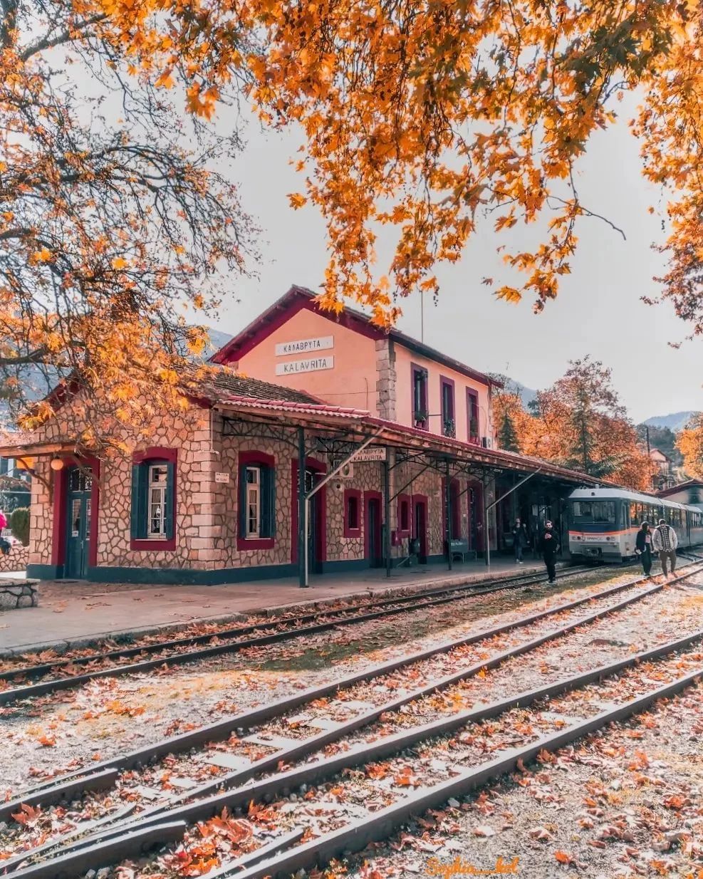 Red brick railway station in Kalavrita with autumn trees and train on tracks