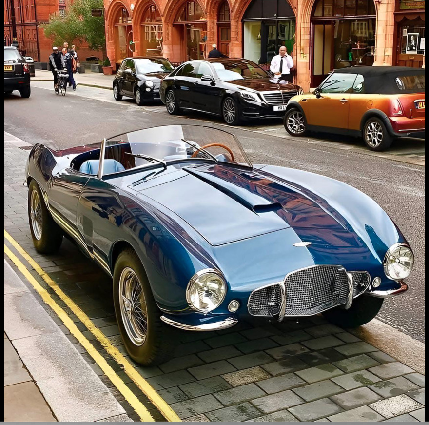 Silver 1954 Aston Martin DB2/4 convertible with blue racing stripes parked on urban street