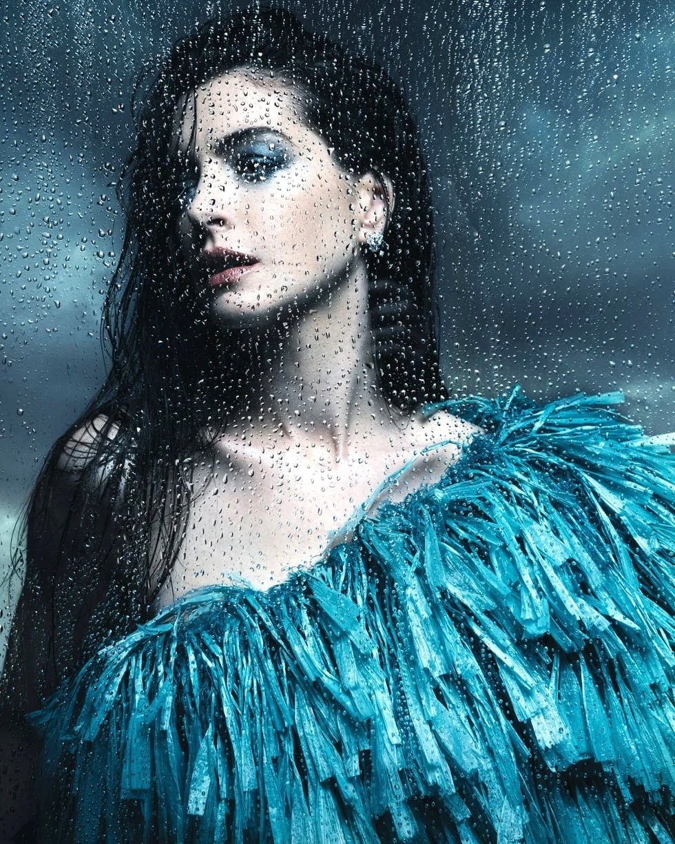 Woman in turquoise feathered dress with long dark hair against blue textured background with water droplets