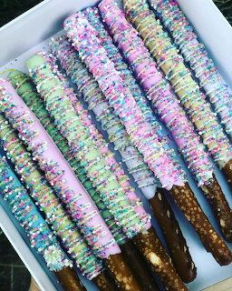 Chocolate-covered pretzel sticks with pastel sprinkles and white chocolate drizzle in a white box