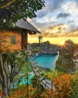 Wooden treehouse with ladder overlooking a turquoise cove and cliffs at sunset