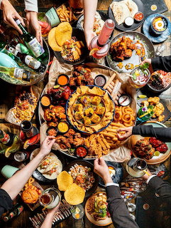 Aerial view of diverse brunch dishes on a table with multiple hands reaching for food