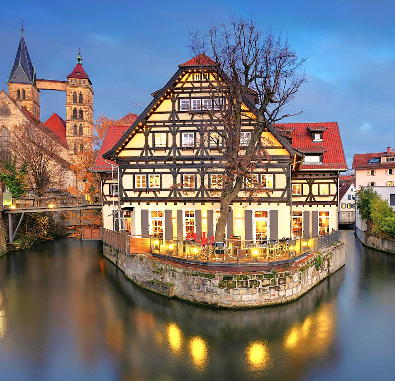 Traditional German half-timbered house on river island at dusk with reflections and church towers behind