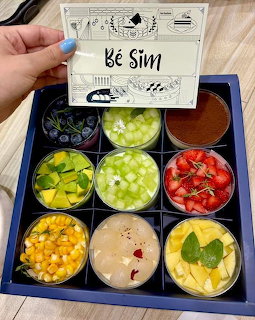 Nine colorful dessert cups in a box with fruit, chocolate, and cream toppings and a label card
