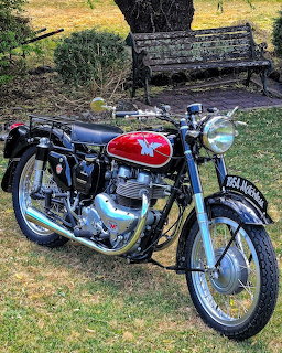 Vintage red and black Matchless motorcycle parked on grass near a bench