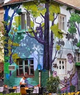 Colorful mural painted across a house exterior with trees, figures, and windows