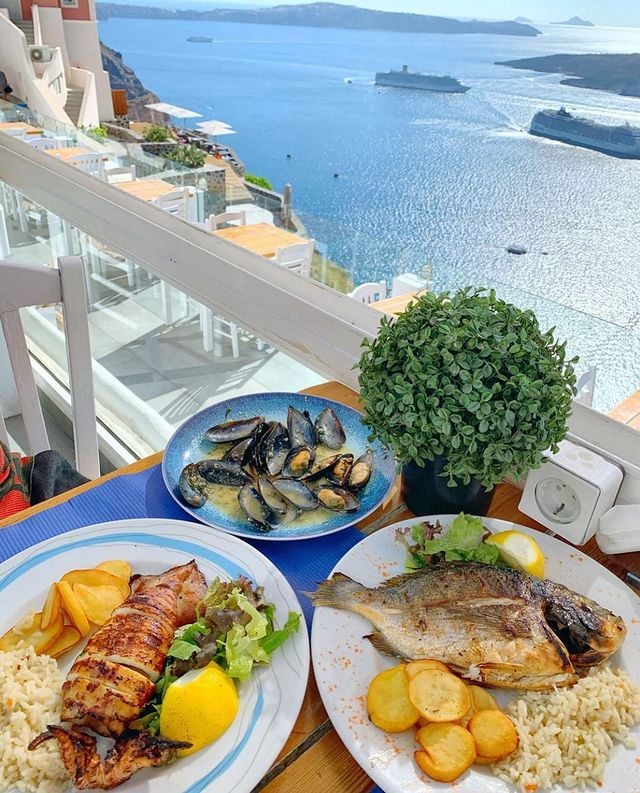 Seafood dishes on table with ocean view and Greek island architecture
