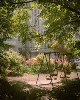 Empty swing set in a green courtyard garden with flowers and trees near an apartment building