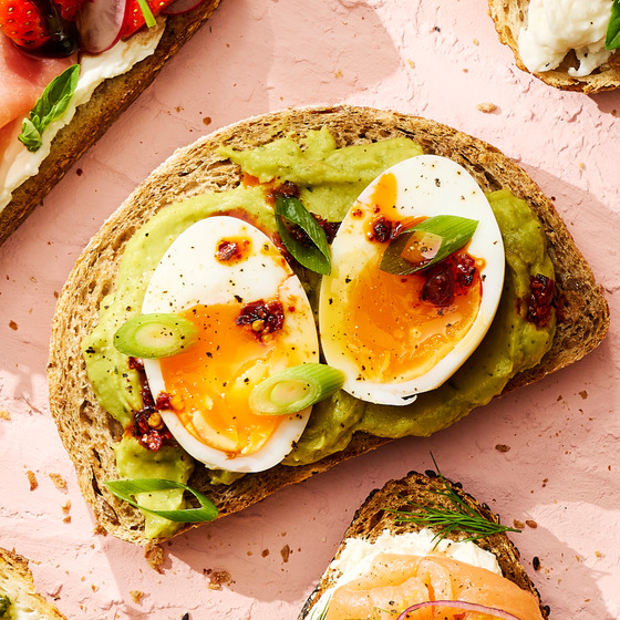 Avocado toast topped with sliced hard-boiled egg and chili flakes on whole grain bread