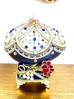 Ornate Fabergé-style Easter egg with blue enamel, gold details, rhinestones, and jewels on a gold stand