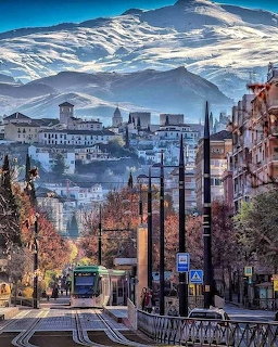 Tram on a Spanish city street with historic buildings and snowy mountains behind