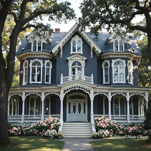 Dark blue Victorian house with white decorative trim and wrap-around porch surrounded by trees and gardens