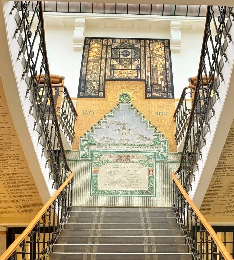 Art Deco staircase with ornate iron railings and decorative tiled walls seen from top landing