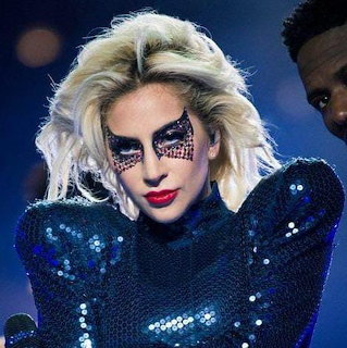Female singer with bold black eye makeup and red lips in a blue sequined outfit performing on stage
