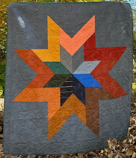 Handmade quilt with geometric star pattern in warm colors on gray fabric