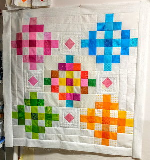 Geometric quilt with five colorful diamond patterns arranged on white quilted fabric