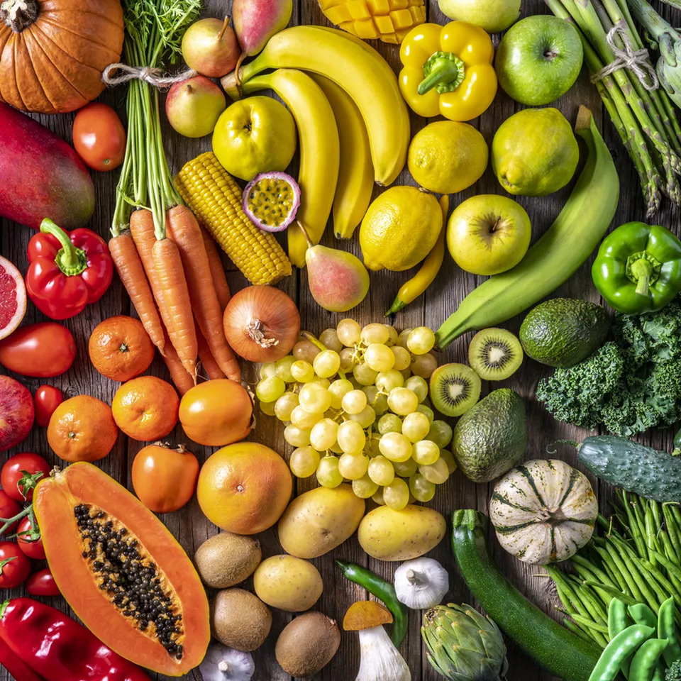 Overhead view of colorful fresh fruits and vegetables arranged in rainbow pattern on white background