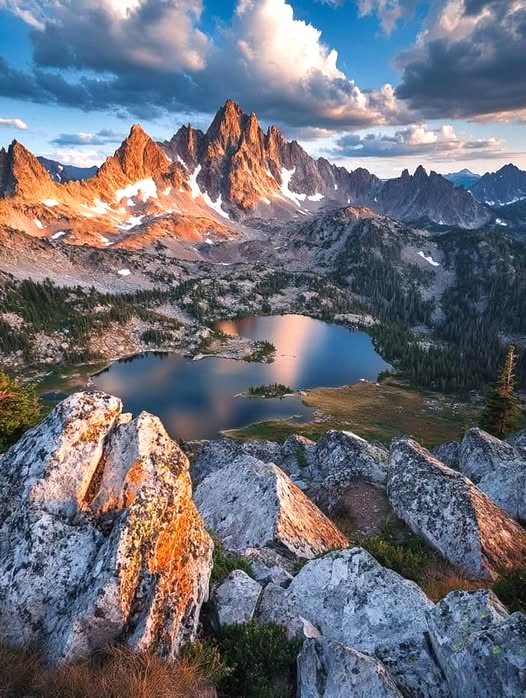Jagged mountain peaks above an alpine lake with rocky foreground and dramatic clouds