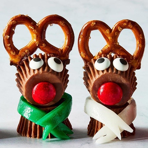 Two chocolate reindeer treats with pretzel antlers, candy eyes, red noses, and colored ribbon scarves