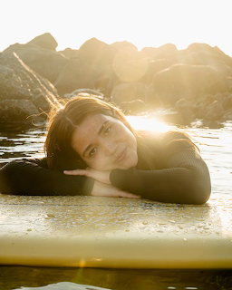 Woman lying on a surfboard in shallow water with sunlit rocks in the background