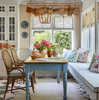 Cozy cottage breakfast nook with farmhouse table, wicker chairs, window seat, and fresh flowers by sunny windows