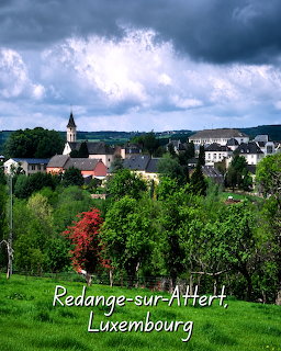 Village view of Redange-sur-Attert, Luxembourg, with church, houses, trees, and cloudy sky