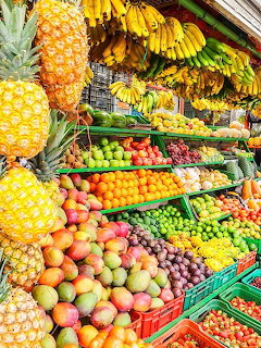 Vibrant tropical fruit market stand with hanging bananas, pineapples, and colorful fresh produce in crates