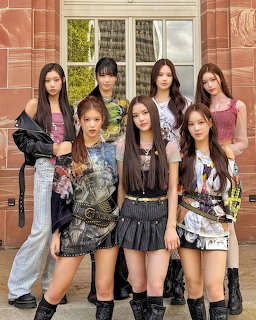 Seven young women in fashionable outfits posing together in front of a classic stone building