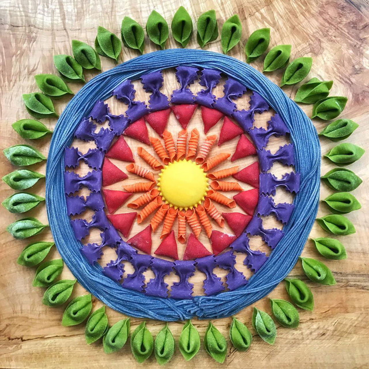 Circular mandala design created with colorful pasta arranged in geometric patterns on a blue plate