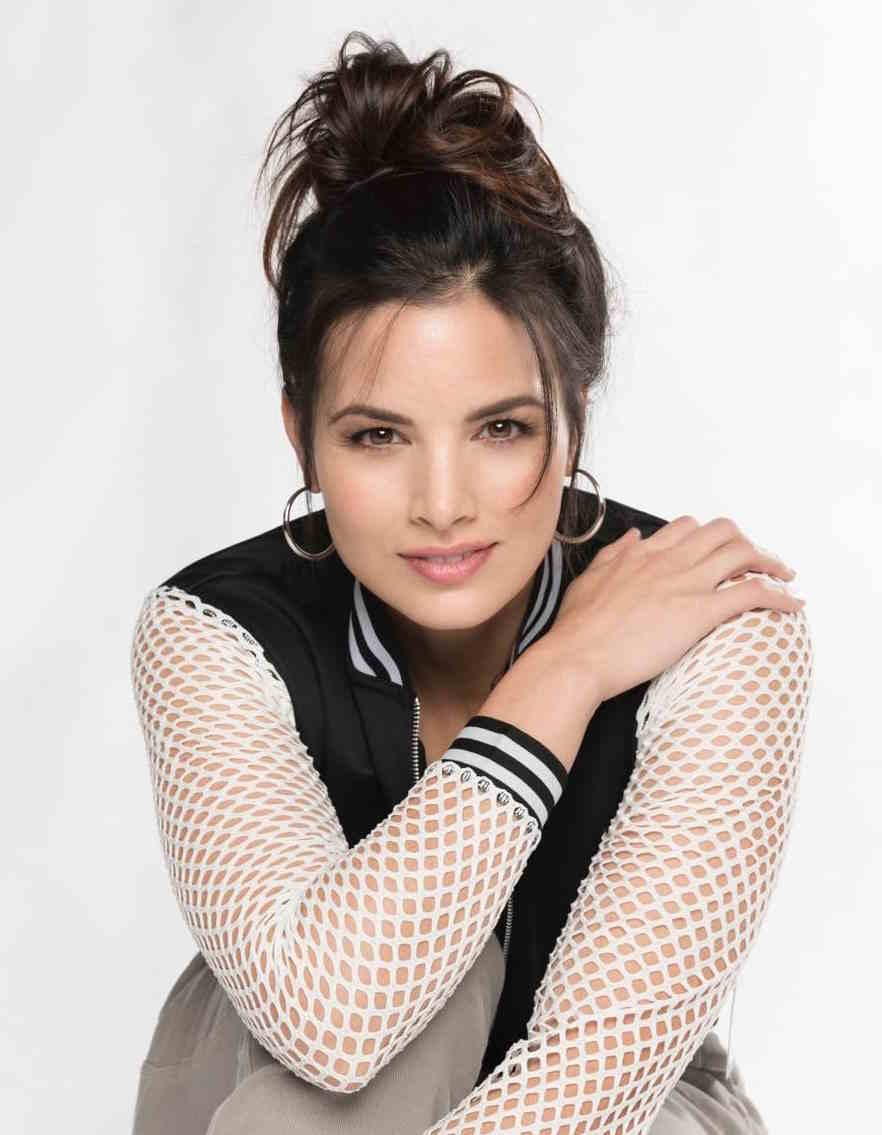Studio portrait of a woman posing with crossed arms, hoop earrings, and white mesh sleeves