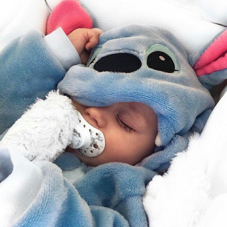 Baby sleeping peacefully in a blue Stitch onesie while holding a small white plush toy