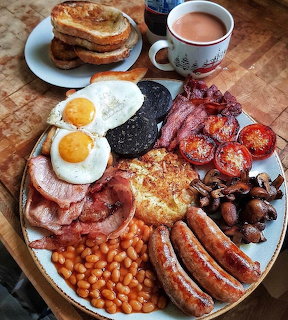 Full English breakfast with eggs, bacon, sausages, beans, and grilled vegetables on a wooden platter