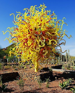 Bright yellow glass tree sculpture in a desert garden beneath a blue sky