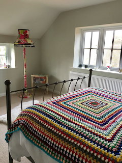 Colorful crochet granny square blanket on iron bed in cozy attic bedroom with vintage lamp