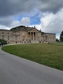 Georgian neoclassical mansion with columned entrance on green lawn under stormy sky