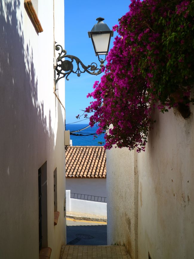 Narrow white alley in Altea, Spain with a street lamp, pink bougainvillea, and sea view