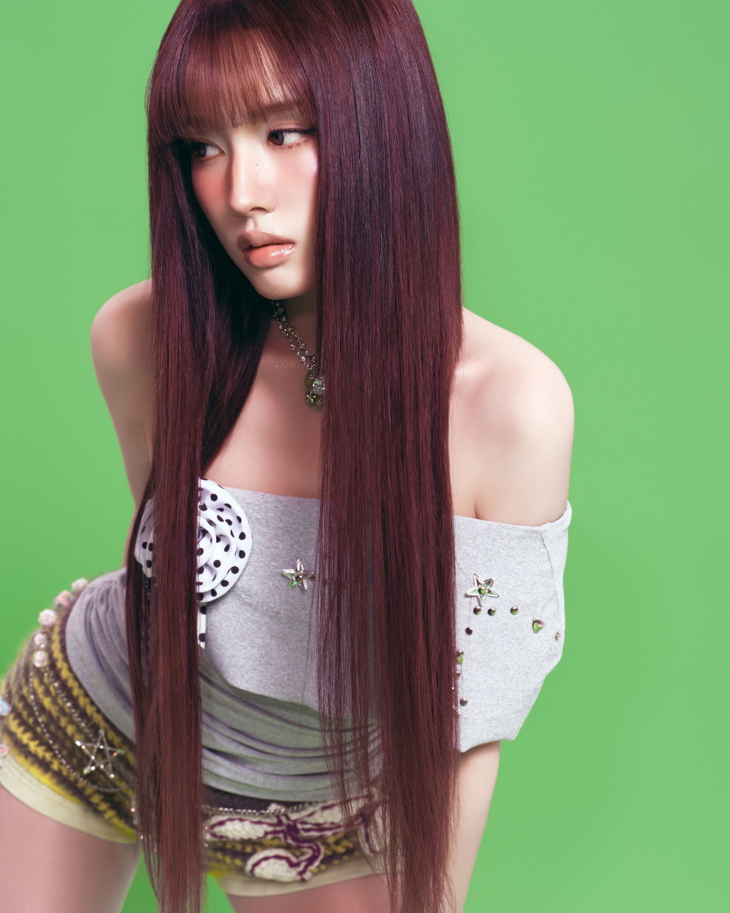 Woman with long purple hair and bangs in white off-shoulder top on green background