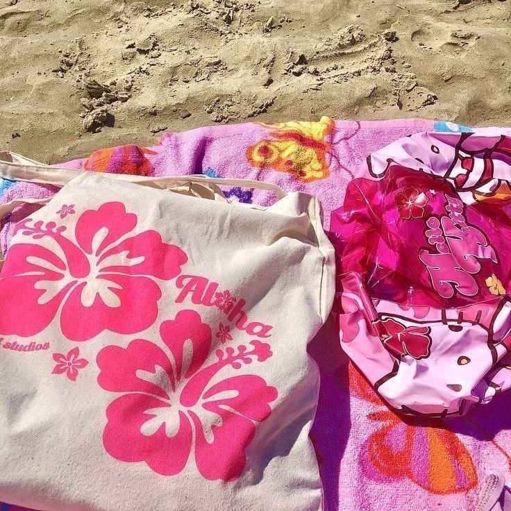 Pink beach towels and a floral tote bag on sand at the beach