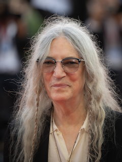 Patti Smith with long gray hair and tinted glasses at an event