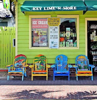 Bright yellow ice cream shop with teal awning and colorful painted chairs on wooden deck