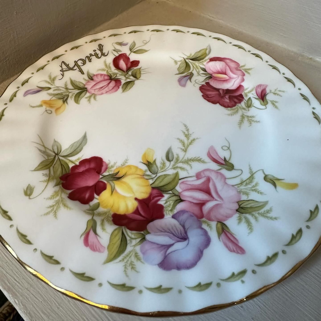White china plate with hand-painted spring flowers and 'April' text, gold scalloped rim
