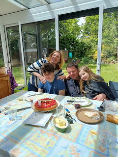 Family of four smiling together at a table with a strawberry tart in a glass conservatory