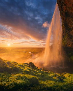 Waterfall flowing over green cliff at sunset with dramatic orange and blue clouds
