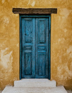 Weathered blue wooden door in a yellow stucco wall with white stone steps