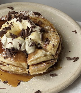 Stack of pancakes topped with whipped cream and chocolate shavings on a ceramic plate