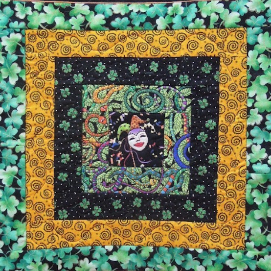 Square quilt with shamrocks, spiral border, and a colorful central clown face panel
